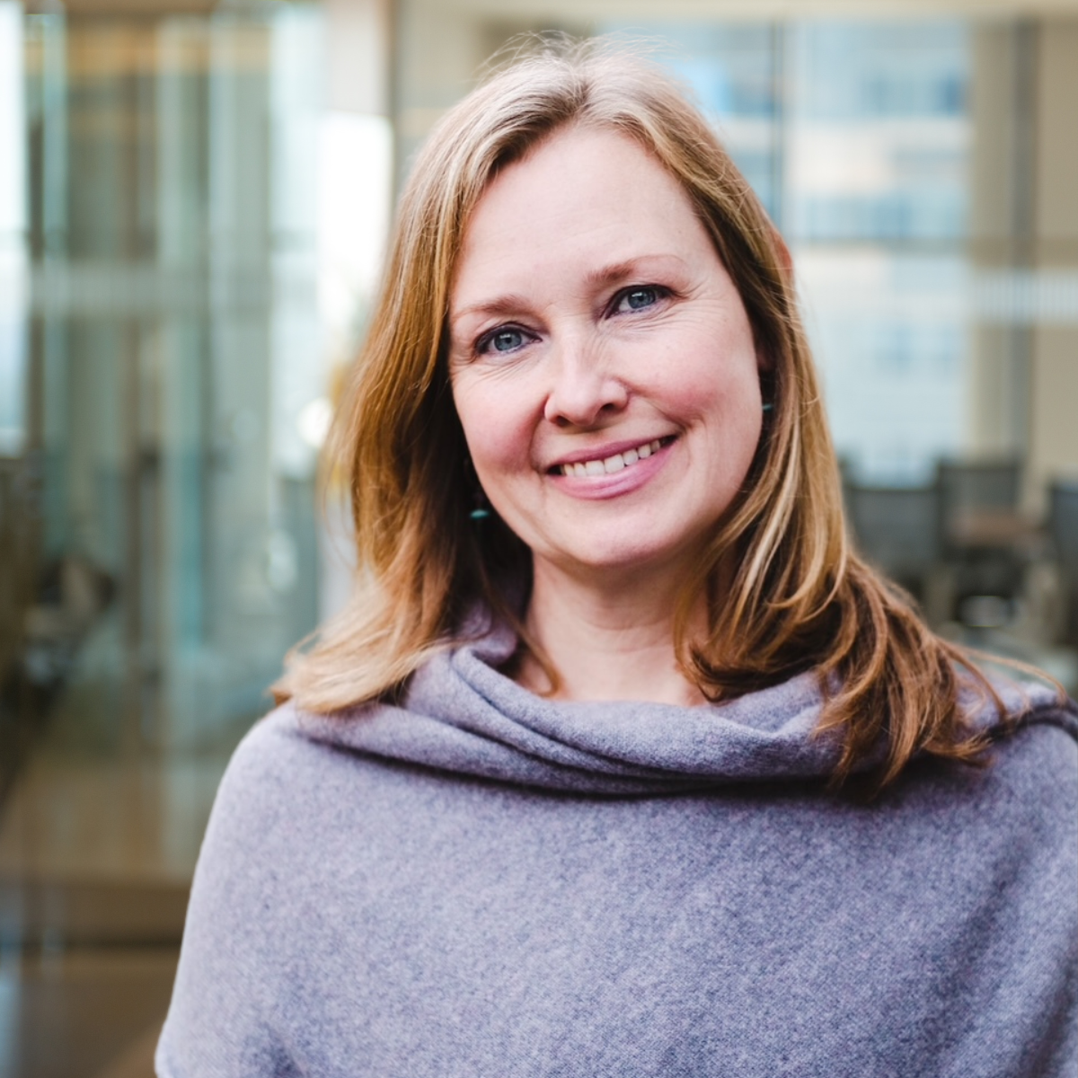 Delphine headshot to centre of image and blurred background of an office in the background with natural light